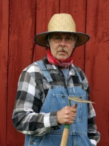 7759241-farmer-holding-a-garden-hoe-wearing-bib-overalls-with-a-barnboard-background-in-vertical-format